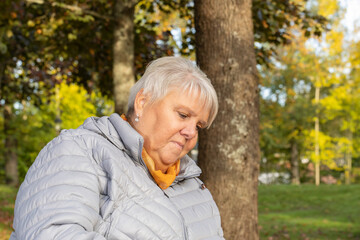 Elderly woman sits on a park bench and enjoys a warm autumn day in the sun