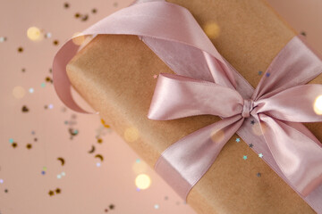 Xmas gift package in kraft paper with pink ribbon on trendy natural beige background with glitter. Zero waste Christmas presents packaging. Happy holidays celebration concept. 2024, 2025 flat lay