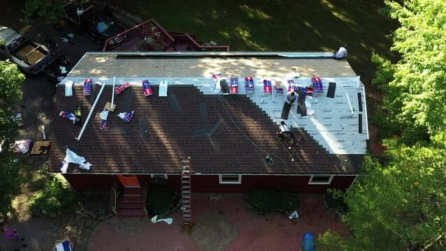 Turning aerial view of laborers nailing new roof shingles as part of a house renovation project