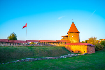 Lithuania, Kaunas castle building and flag in warm sunset light, ancient red brick wall and tower