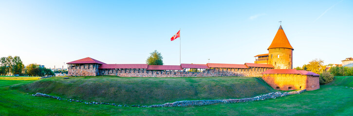 Lithuania, XXL panorama kaunas castle building and flag in warm sunset light, ancient red brick wall and tower