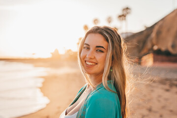 Portrait of one happy beautiful woman on the sand of the beach enjoying and having fun at the sunset of the day. Looking at the camera smiling..