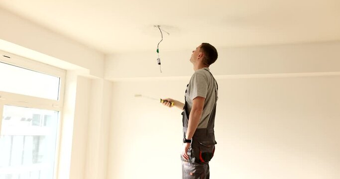 Man paints ceiling white with roller in room. Painting ceiling walls stages and nuances of process