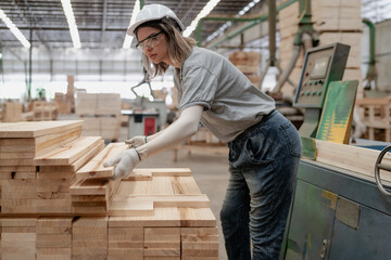 Confident female worker working in lumber warehouse of wooden furniture factory checking stock. Confident skilled inspector wears safety hardhat examining hardwood material for production facility.