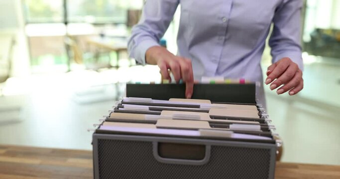 Woman hands take folders with work materials in office. Female accountant looking for accounting documents in archive box