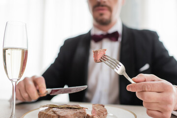 cropped view of wealthy gentleman in tuxedo holding cutlery with tasty cooked beef steak, close up
