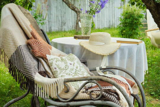 serene backyard, a rocking chair with a blanket invites relaxation, paired with a table hosting bluebells, a straw hat, and a book. A tranquil escape from urban chaos.