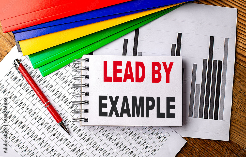 Poster lead by example text on a notebook with pen, folder on a chart background