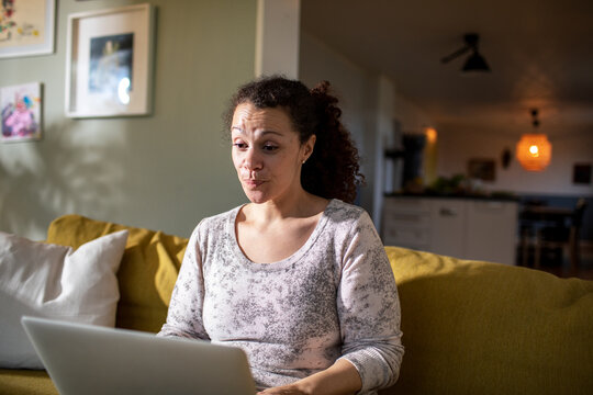 Young mixed woman using a laptop on the couch at home
