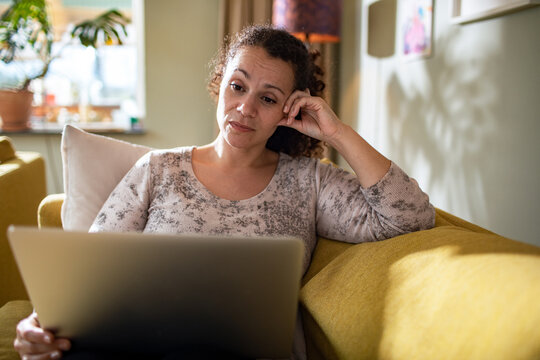 Young mixed woman using a laptop on the couch at home