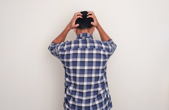 Back view of a man bowed down listlessly with hands grabbing his hair