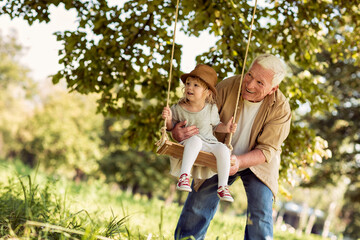 Grandfather pushing granddaughter on the swing in a outdoor park