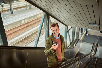 Middle aged man using his smartphone while on the escalator at the train station