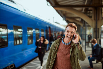 Middle aged man talking on his smartphone while waiting for the train at the train station
