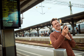 Fototapeta premium Middle aged man using his smartphone while waiting for the train at the train station