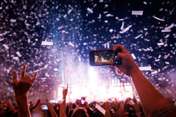 Happy people on the dance floor record a big music concert using a mobile phone. Confetti over raised hands.