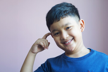 Cute Asian boy six years old pointing finger at head and smile happily having curious look, trying to remember something.