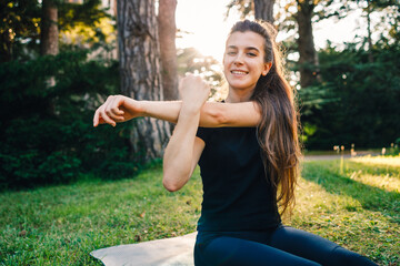 young cute girl doing stretching on the grass in the park. green summer or spring park in the background