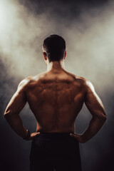 Muscular back of an athlete against a background of smoke