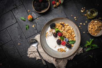 Bowl of homemade granola with yogurt and fresh berries on black background from top view