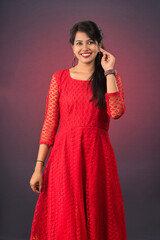 Portrait of a beautiful, smiling, young Indian girl wearing a red dress posing on a dark background