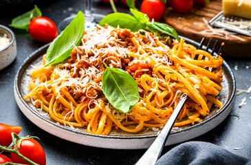 Spaghetti bolognese or pasta with minced meat in tomato sauce with green basil and chianti red wine glass, black table background, top view