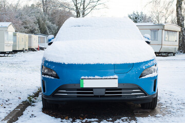 Blue electric car with green numberplate stripe with snow on the bonnet