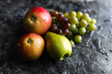 Apples, pears, green and purple grapes lie on a dark background. Organic fruit close-up. Fruits on a black background. Wet washed fruits on a black marble table