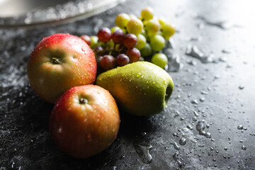 Apples, pears, green and purple grapes lie on a dark background. Organic fruit close-up. Fruits on a black background. Wet washed fruits on a black marble table