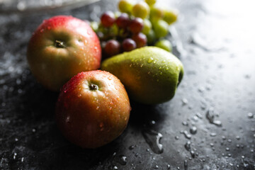 Apples, pears, green and purple grapes lie on a dark background. Organic fruit close-up. Fruits on a black background. Wet washed fruits on a black marble table