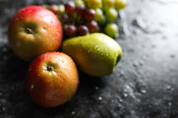 Apples, pears, green and purple grapes lie on a dark background. Organic fruit close-up. Fruits on a black background. Wet washed fruits on a black marble table
