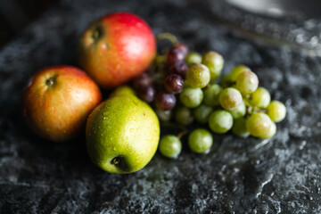 Apples, pears, green and purple grapes lie on a dark background. Organic fruit close-up. Fruits on a black background. Wet washed fruits on a black marble table