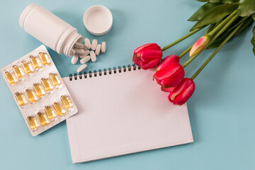 Transparent capsules with fish oil, notepad, blister, capsules and flowers on a blue background....