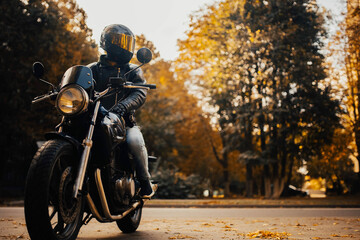 motorcyclist in a helmet with a classic motorcycle in the fall. Stylish motorcyclist in a leather...