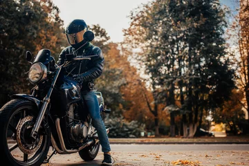 Photo sur Plexiglas Moto motorcyclist in a helmet with a classic motorcycle in the fall. Stylish motorcyclist in a leather jacket and gloves.
