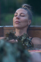 A young woman in a swimsuit sits in a sauna vat with herbs. The beauty enjoys water treatments. Spa...