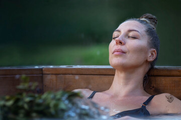 A young woman in a swimsuit sits in a sauna vat with herbs. The beauty enjoys water treatments. Spa...