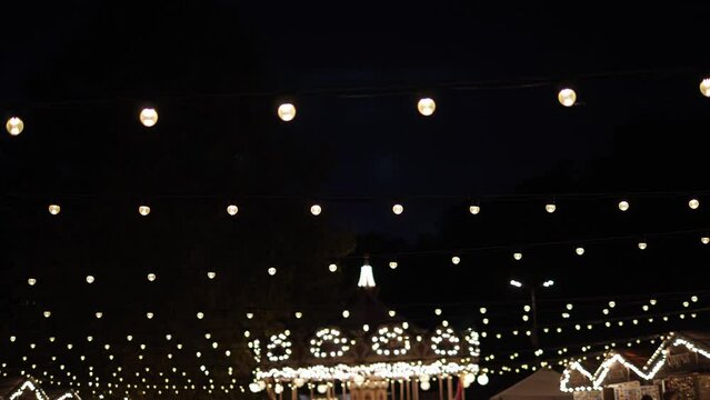 Hanging rows of garlands with light bulbs and a rotating carousel in the evening at an amusement park. A bright glowing carousel in the dark.