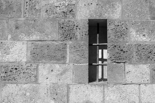 Pequeña ventana con rejas en un muro de un edificio medieval en blanco y negro