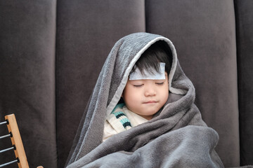 Asian boy Lying sick, he had a fever reducing patch on his forehead and covered himself with a blanket because of the cold.