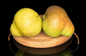 Two organic green pears on a wooden round tray, close-up, isolated on black.