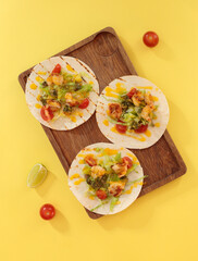 tortillas with vegetables and meat on a wooden board. On a yellow background, top view.