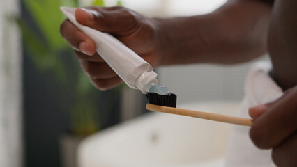 Close up hands squeezing out white toothpaste from tube on toothbrush dental care morning procedure oral hygiene prevent tooth caries unknown African American man prepare brushing teeth in bathroom