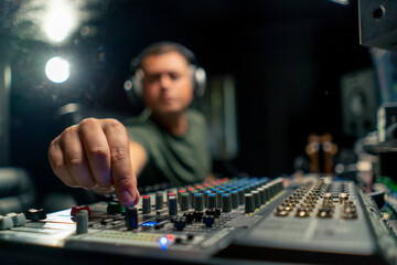 Concentrated male sound engineer working at the mixing console in a music studio to record a soundtrack