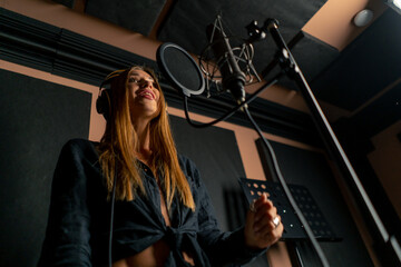 girl singer singing in a recording studio with headphones in front of microphone to create a new song