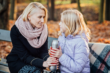 Creative Kid-Friendly Picnic Ideas For Autumn. Happy mother with teenager daughter with blanket and thermos on fall picnic. Mom and daughter picnic in the autumn park - obrazy, fototapety, plakaty