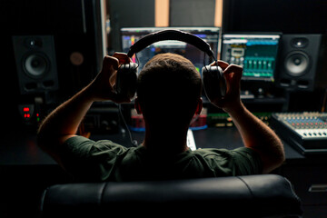 a male sound engineer sits at a mixing desk with his back to camera and puts on headphones