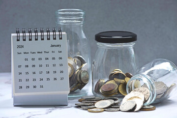 January 2024 calendar and glass jars with multicurrency coins.