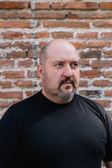 Fototapeta premium Exterior close-up of a 45-year-old bald man with a goatee and mustache looking to the right against a brick background