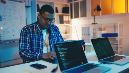 African American man testing software in office at night, IT support, programmer